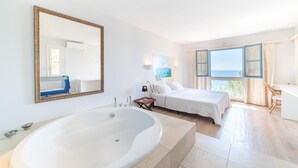Une chambre d’hôtel moderne dotée d’une grande baignoire, d’un lit, d’un bureau et offrant une vue sur la mer.