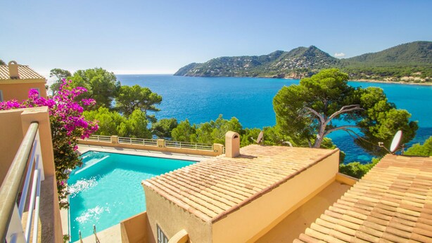 Une vue sur la piscine, avec une mer d’un bleu limpide et une chaîne de montagnes en arrière-plan.