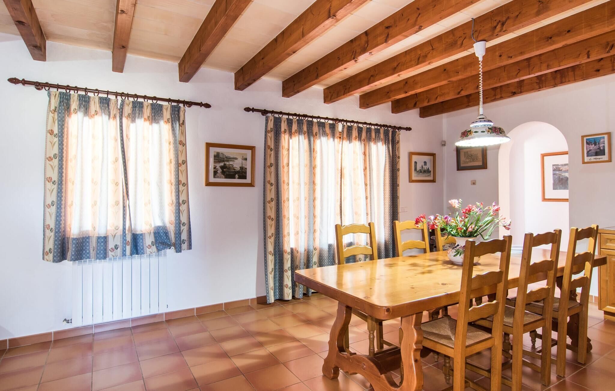 A dining area with a wooden table and chairs, two windows with curtains, and a hanging light fixture.