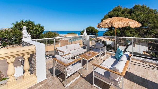 A terrace with outdoor seating, a thatched umbrella, and a view of the sea. - Beautiful home in Sa Font de Sa Cala (Sa Font de Sa Cala)