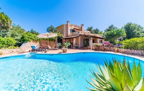 Une villa de style méditerranéen dotée d’une piscine, d’un espace salon extérieur et d’une végétation luxuriante.