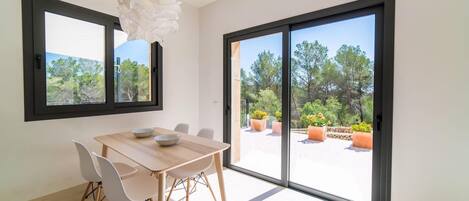 Un'area pranzo moderna con tavolo e sedie in legno, ampie finestre e vista sull'esterno.