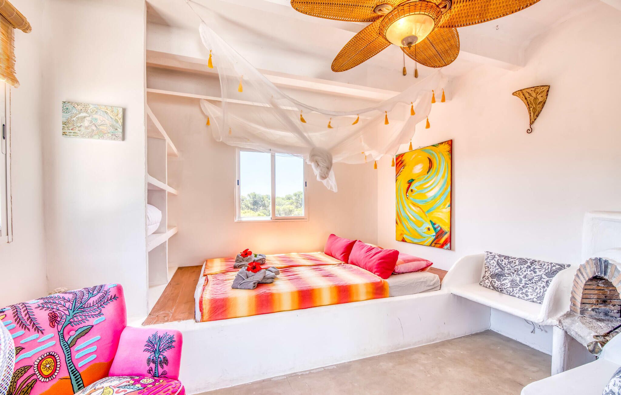 Un dormitorio luminoso y espacioso con cama, almohadas, una silla blanca, una mesita y un estante en la pared.