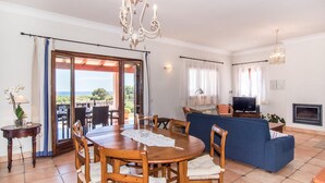 Amplia sala de estar con mesa de comedor, sillas, sofá, televisor y chimenea.