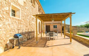 Een stenen gebouw met een overdekte patio, voorzien van een barbecue, buitenmeubels en een pergola.