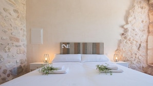 Ein Schlafzimmer mit einem großen Bett, zwei Nachttischen mit Lampen, einem Holz-Kopfteil und Steinwänden.