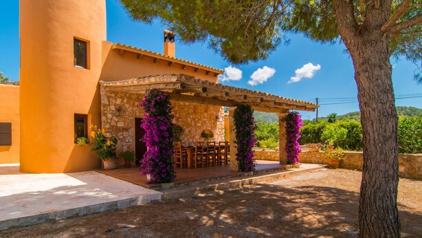 A building with a stone facade, a covered patio with a table and chairs, and a pergola with purple flowers. - Stunning home in Felanitx with private swimming pool, can be inside or outside (Felanitx)