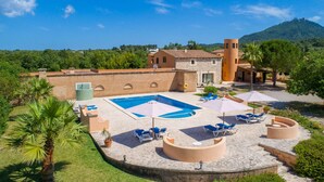 A pool area with lounge chairs and umbrellas, surrounded by stone buildings and palm trees. - Stunning home in Felanitx with private swimming pool, can be inside or outside (Felanitx)