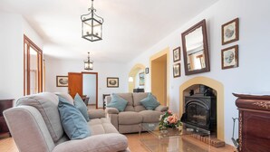 Een woonkamer met twee banken, een glazen salontafel, een open haard en ingelijste foto's aan de muur.