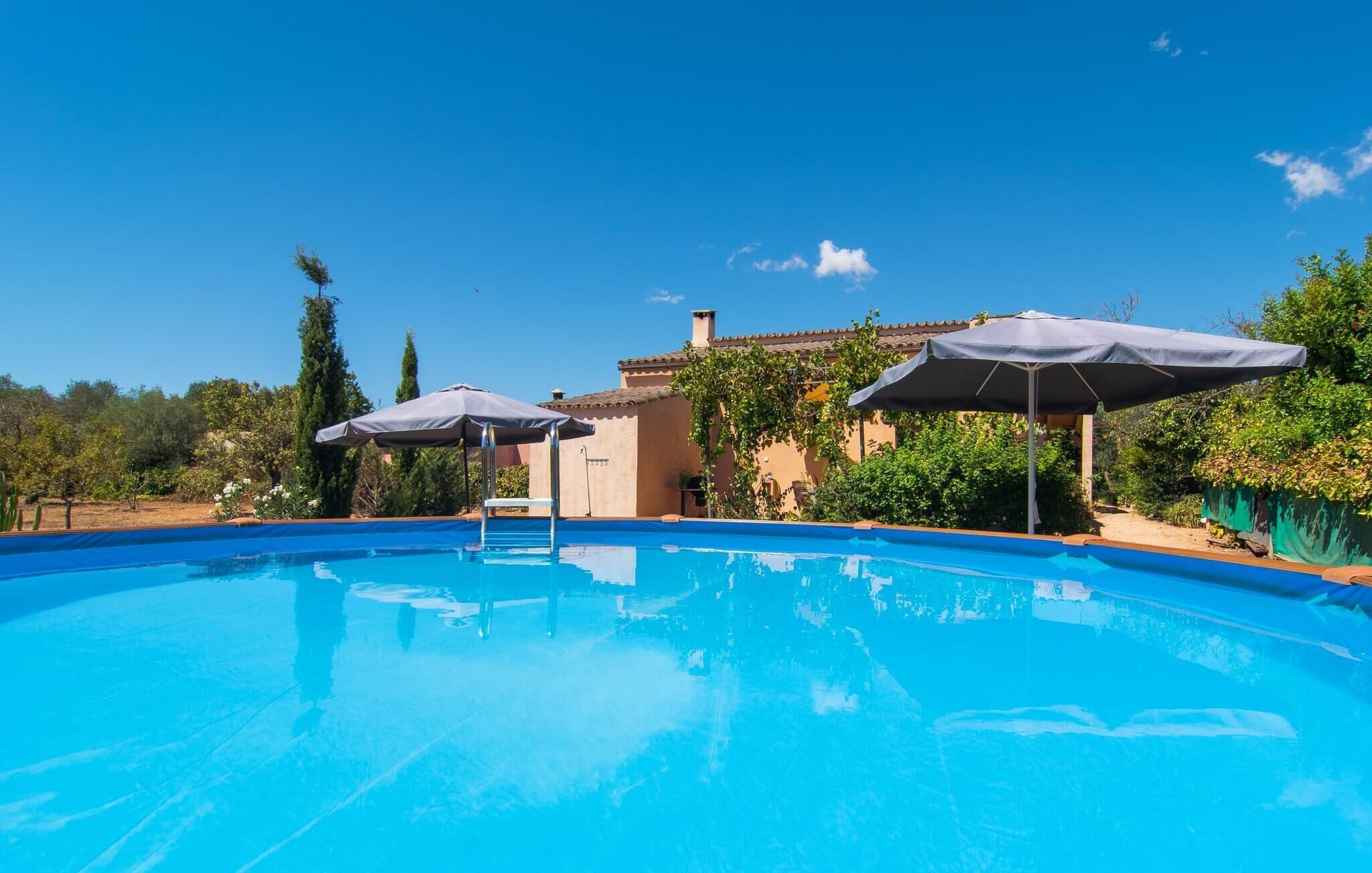Una piscina azul cristalina con dos sombrillas, rodeada de vegetación y un edificio con tejado de baldosas.