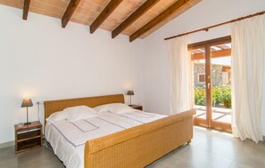 Ein Schlafzimmer mit einem hölzernen Bett, weißer Bettwäsche, zwei Nachttischlampen und Blick auf einen Garten durch eine Glastür.