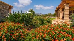 A stone building with a garden in front, featuring red flowers and green plants. - Lovely home in Arta with private swimming pool, can be inside or outside (Arta)