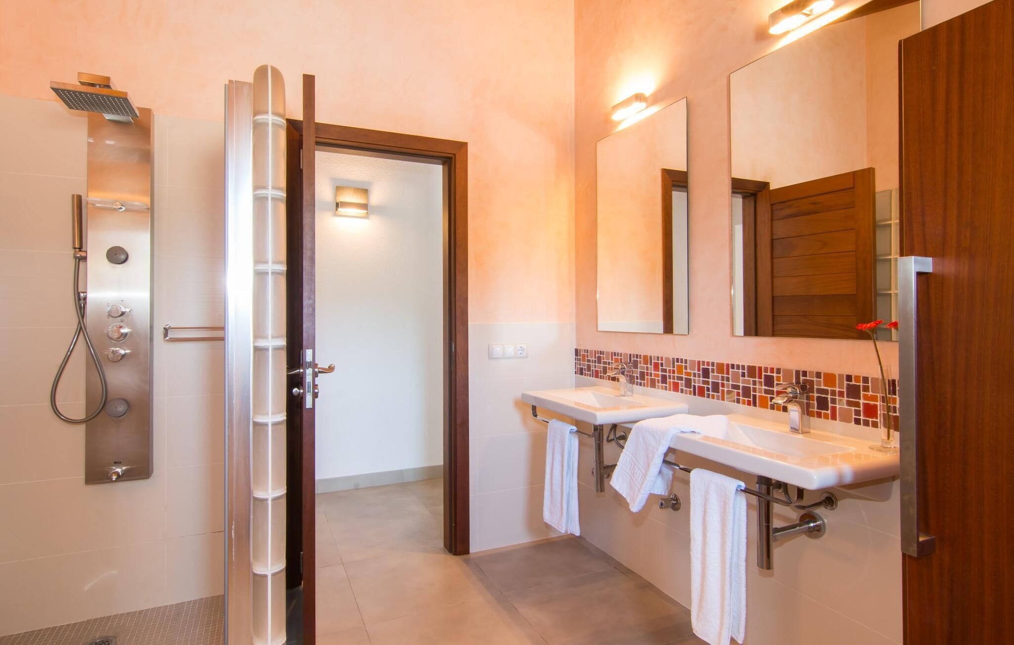 Ein modernes Badezimmer mit Dusche, zwei Waschbecken und einem großen Spiegel.