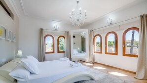 Un dormitorio con una cama grande, una araña y tres ventanas de arco.