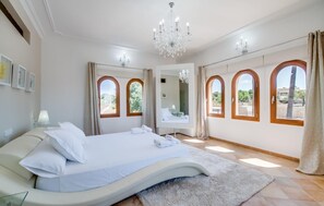 A bedroom with a large bed, a chandelier, and three arched windows.