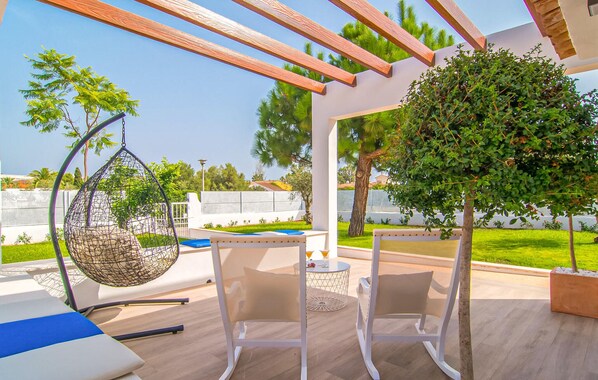 Een terras met een hangstoel, twee stoelen, een tafel en een kleine boom.