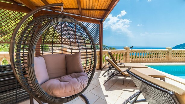 Ein Korbstuhl mit Kissen, ein Poolbereich mit Liegestühlen und Blick aufs Meer.