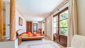 Ein Schlafzimmer mit Bett, Stuhl, Schreibtisch und Fenster mit Blick ins Grüne.
