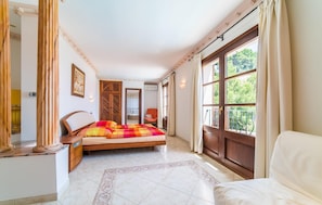 A bedroom with a bed, a chair, a desk, and a window with a view of greenery. - Lovely home in Canyamel with private swimming pool, can be inside or outside (Canyamel)