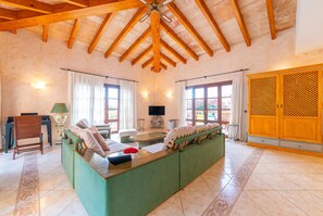 A spacious living area with a high ceiling, a green sofa set, a wooden coffee table, and a television. - Lovely home in Canyamel with private swimming pool, can be inside or outside (Canyamel)