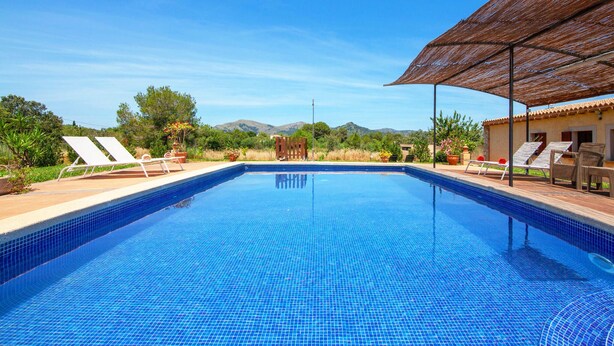 Ein Swimmingpool mit blau gefliestem Boden, umgeben von Liegestühlen und einem überdachten Bereich mit einem Reetdach.