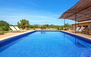 Une piscine dont le fond est recouvert de carreaux bleus, entourée de chaises longues et d’un espace abrité avec un toit de chaume.