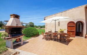 Une terrasse extérieure avec un barbecue en briques, une table avec des chaises et un grand parasol pour faire de l’ombre.