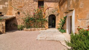 Une cour bordée de murs en pierre, avec une arche centrale et un chemin de gravier menant à une porte.