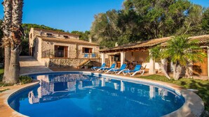Un'area piscina con un edificio in pietra, un portico coperto e un cielo azzurro intenso.