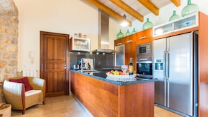 A kitchen with wooden cabinets, a stainless steel refrigerator, a built-in oven, and a stone wall. - Stunning home in Inca with private swimming pool, can be inside or outside (Inca)