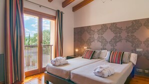 A hotel room with two beds, a balcony with curtains, a patterned wall, and wooden floors. - Nice home in Pollenca with private swimming pool, can be inside or outside (Pollenca)