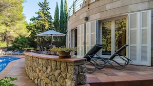 A poolside area with a stone wall, lounge chairs, a table with umbrellas, and a view of the pool. - Beautiful home in Alcudia with private swimming pool, can be inside or outside (Alcudia)