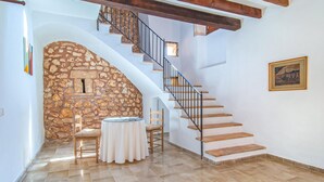 A room with a stone wall, a wooden chair, a round table, and a staircase with a metal railing. - Awesome home in Porto Cristo (Porto Cristo)