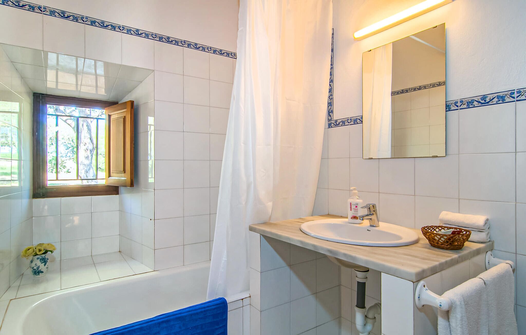 Une salle de bain avec une baignoire, un lavabo, un miroir et une fenêtre donnant sur les arbres.