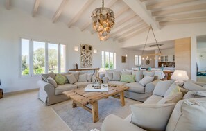 Un salon spacieux avec une table basse en bois, des canapés de couleur beige et un lustre original.
