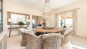 A dining area with wicker chairs, a round wooden table, and a chandelier. - Nice home in Alqueria Blanca (Alqueria Blanca)