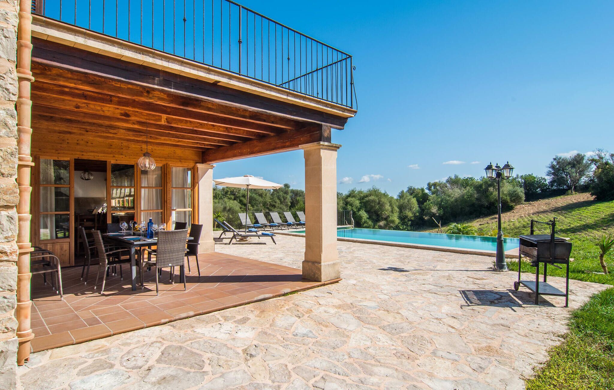 Un patio de piedra con piscina, mobiliario de exterior y una zona cubierta con mesas y sillas.