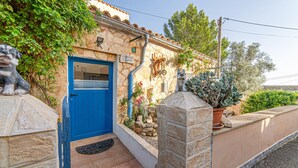 A stone building with a blue door, a stone wall, and a small garden with plants and a statue. - Pet friendly home in Galilea (Galilea)