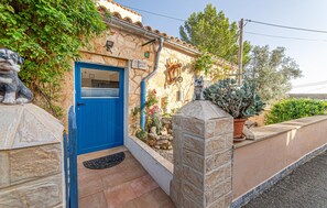 A stone building with a blue door, a stone wall, and a small garden with plants and a statue. - Pet friendly home in Galilea (Galilea)