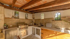 A rustic kitchen with a stone backsplash, wooden beams, a built-in grill, and a stone countertop. - Pet friendly home in Galilea (Galilea)