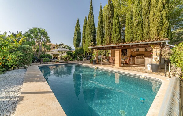 A swimming pool with a pergola and outdoor kitchen area, surrounded by tall trees and potted plants. - Pet friendly home in Galilea (Galilea)