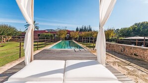 A pool area with a wooden deck, white canopies, and a view of a landscaped garden with trees and a building in the background. - Nice home in Manacor with sauna (Manacor)
