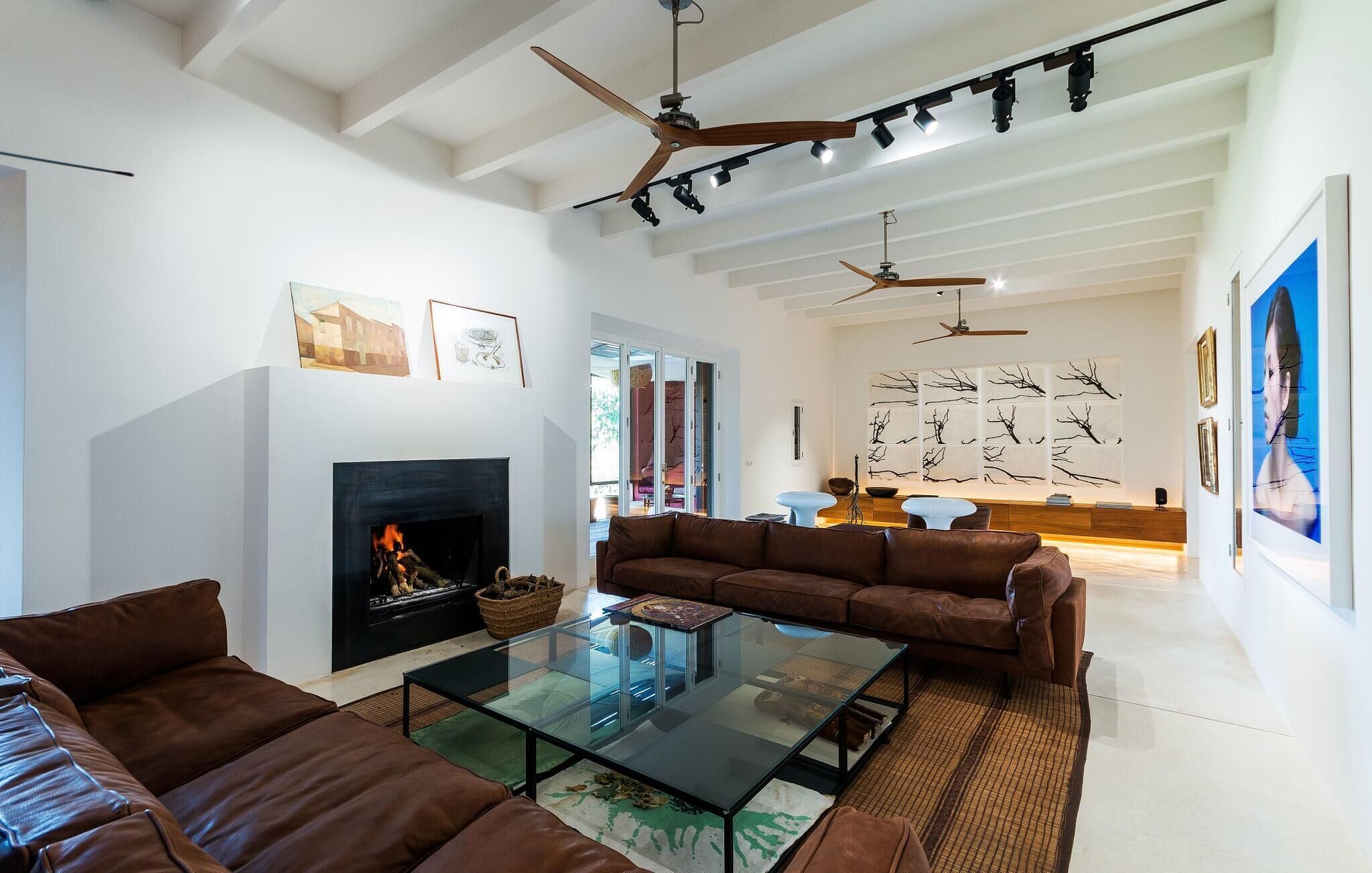Ein geräumiges Wohnzimmer mit Kamin, Ledersofas, einem Glastisch und Deckenventilatoren.