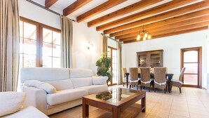 Un salon spacieux comprenant un canapé, une table basse et un coin repas avec des chaises en osier.