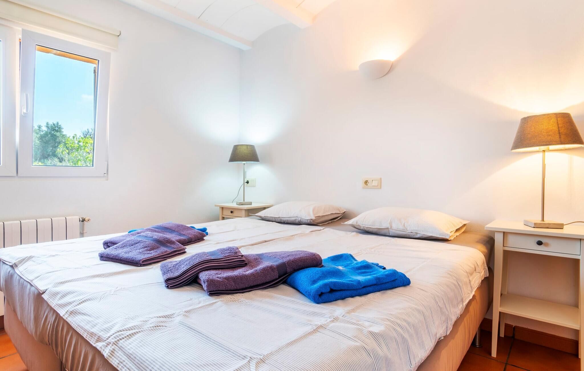 Ein Schlafzimmer mit einem Bett, zwei Nachttischen, einem Fenster, einer Heizung und einer Lampe.