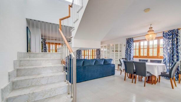 A spacious living area with a marble staircase, a blue sofa, a dining table with chairs, and a chandelier. - Stunning home in Cala dOr with private swimming pool, can be inside or outside (Cala dOr)