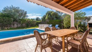 A covered outdoor area with a pool, a wooden table, and wicker chairs. - Stunning home in Cala dOr with private swimming pool, can be inside or outside (Cala dOr)