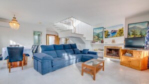 A modern living room with a blue sectional sofa, a glass coffee table, a fireplace, a TV, and a staircase leading to an upper level. - Stunning home in Cala dOr with private swimming pool, can be inside or outside (Cala dOr)
