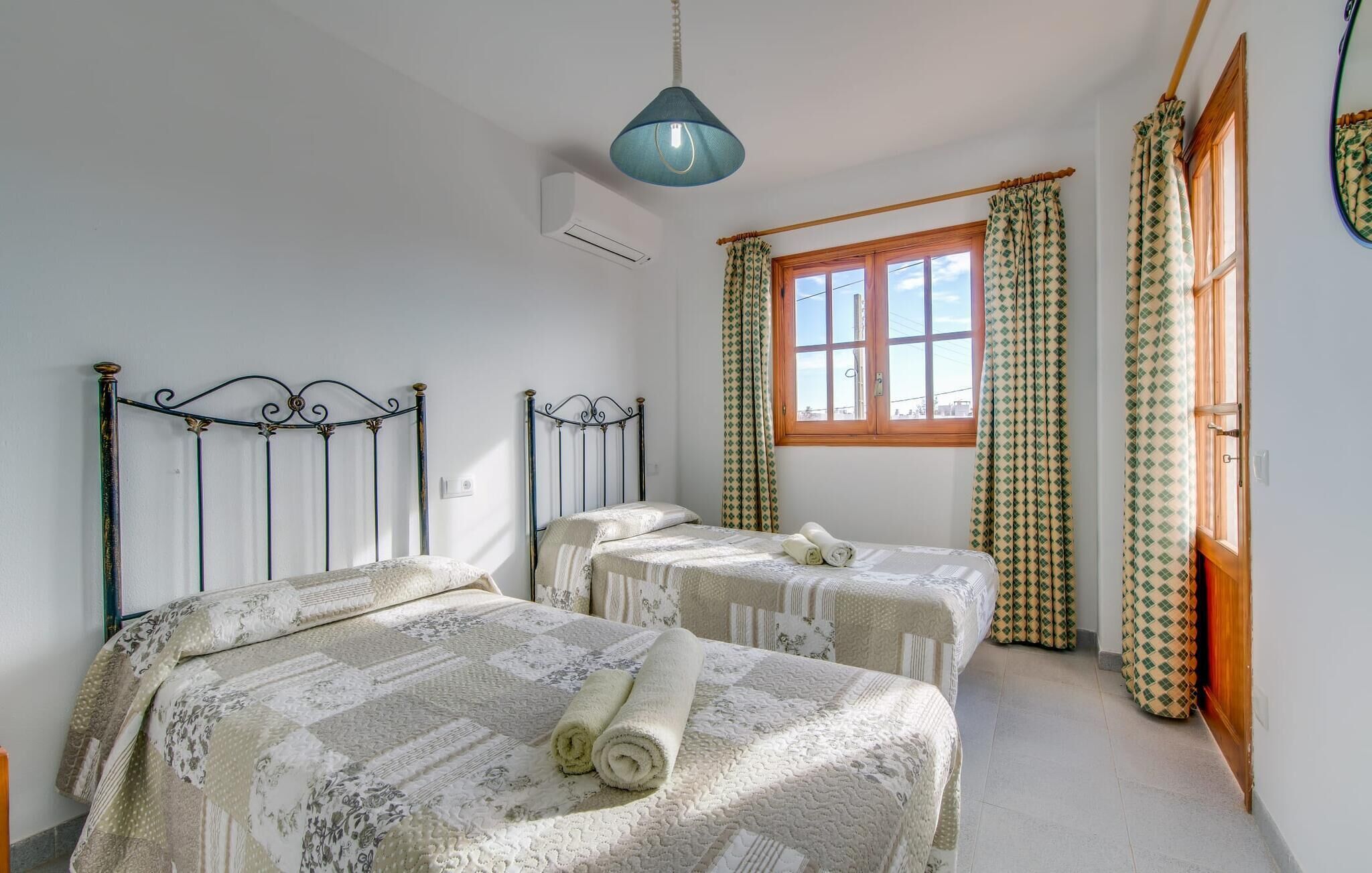 Een slaapkamer met twee bedden, een raam met gordijnen en een hanglamp.