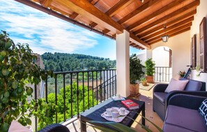 A balcony with a view of a forested area, a wicker sofa, and a table with cups and a book. - Stunning home in Selva with private swimming pool, can be inside or outside (Selva)